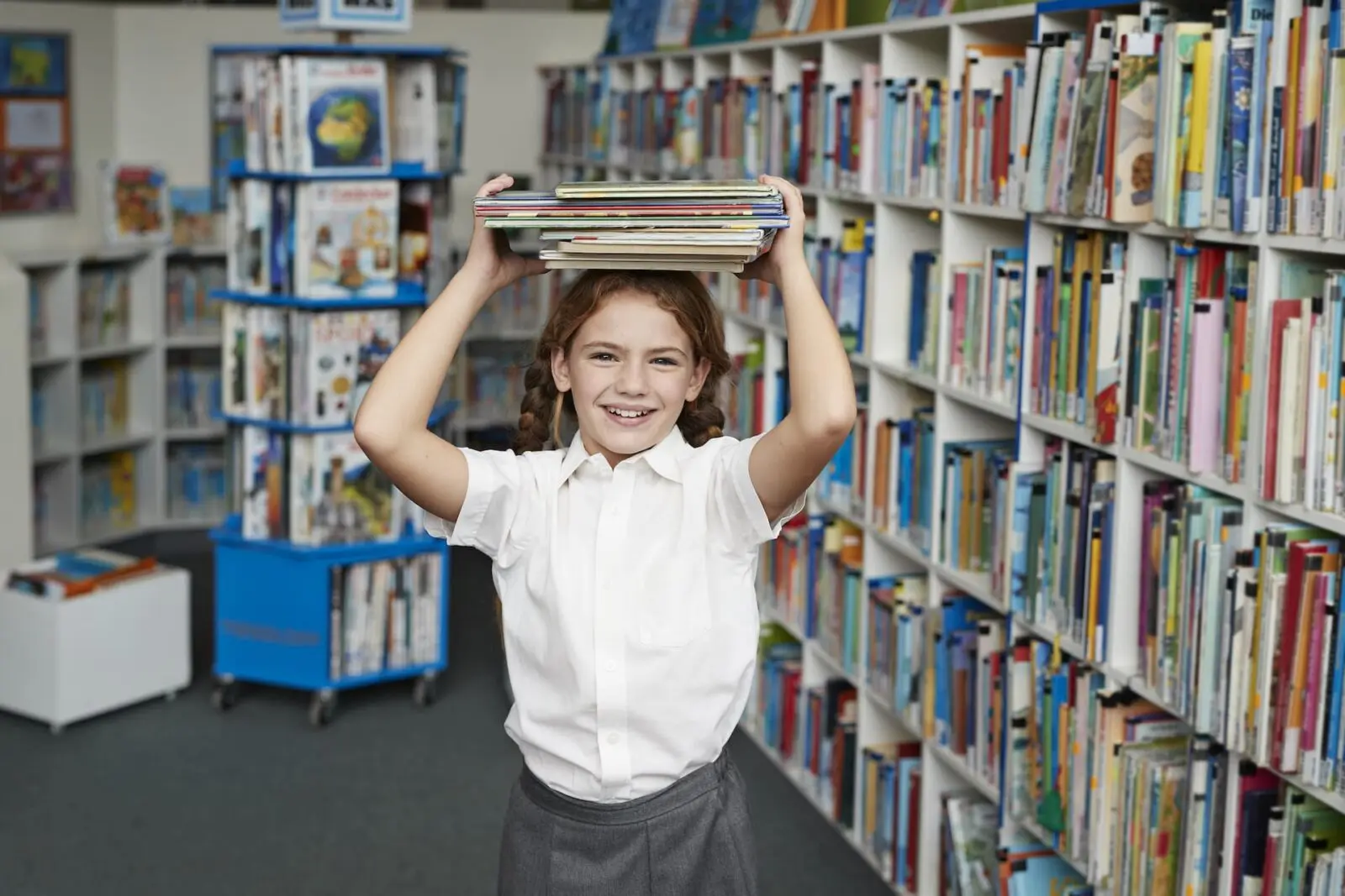 Girl holding books over her head in a library